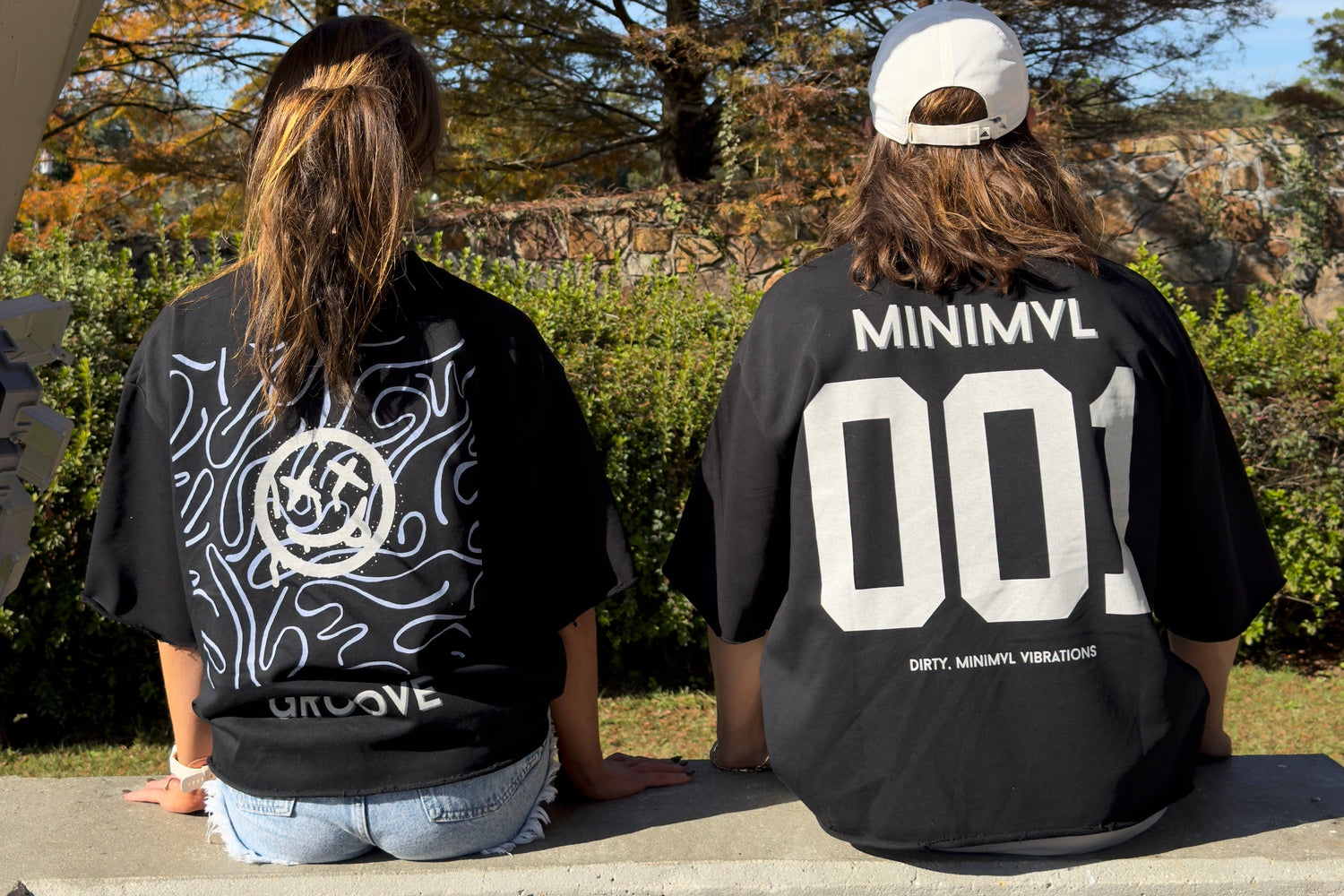 Two people wearing black t-shirts with visible branding sitting on a bench outdoors.